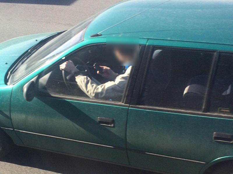 Condutor de carro verde segurando o celular enquanto dirige, visto de cima