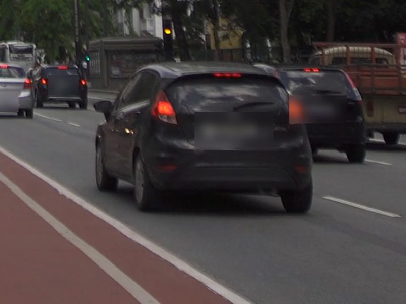 Carro escuro trafegando em avenida, visto de trás, marcado pela IA