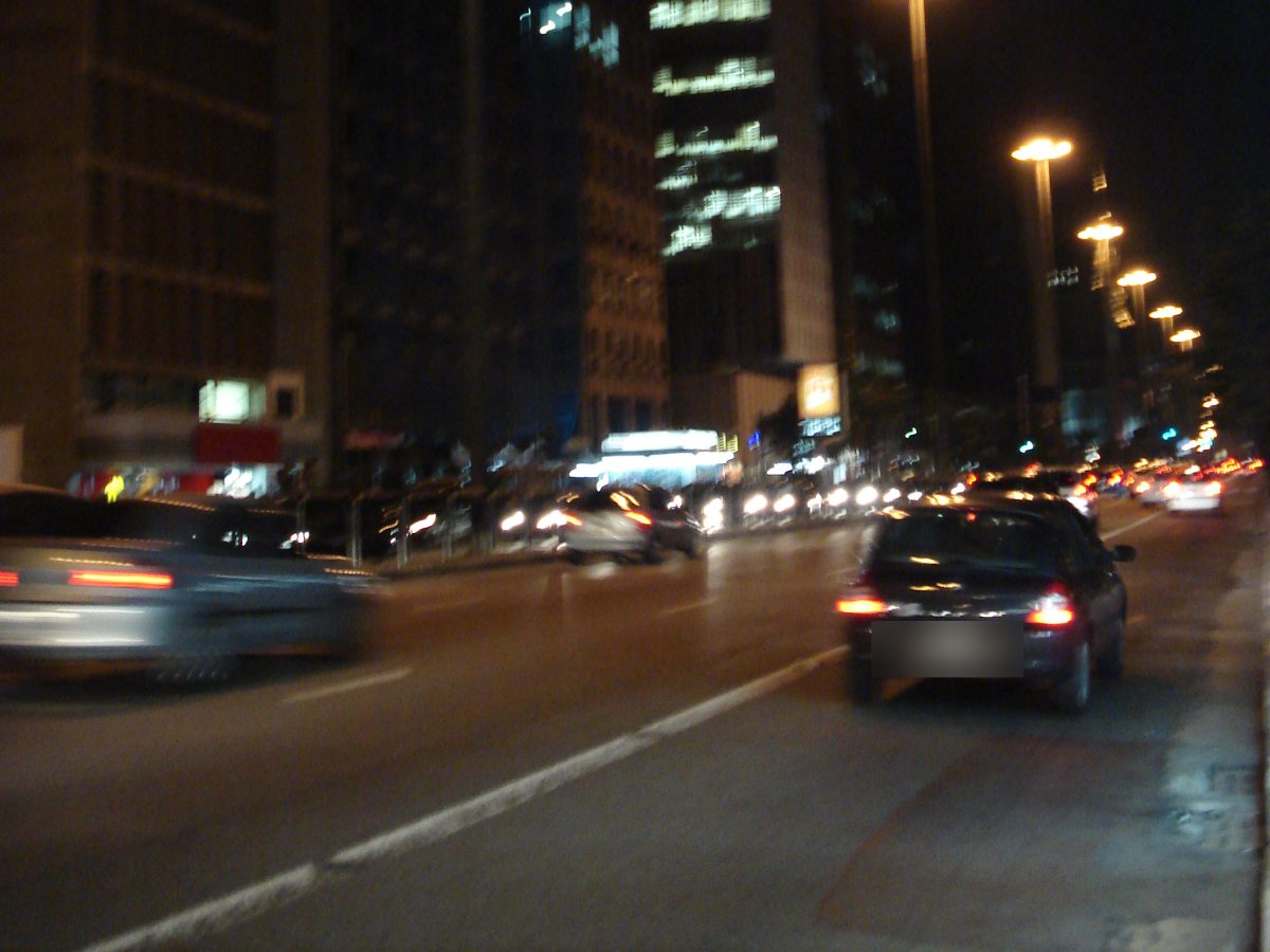 Avenida à noite vista da pista, com faróis e lanternas dos carros